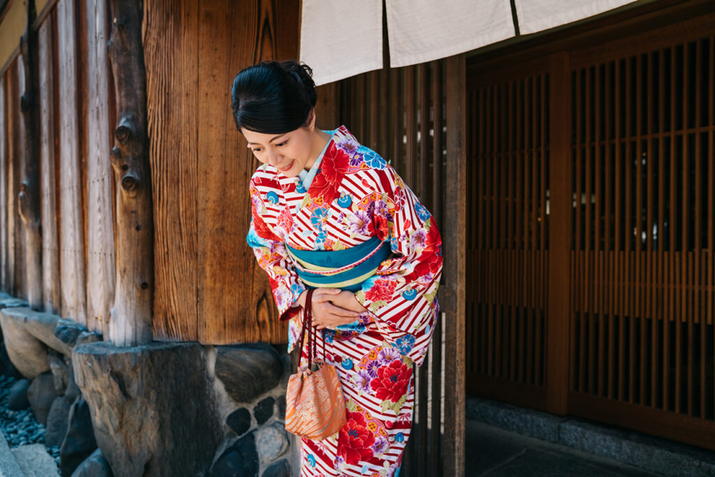 Japanese lady bowing in front of her house with beautiful kimono. traditional lifestyle in jp. attractive woman with colorful kimono clothing in summer.